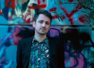 Literatur in Göteborg und Stockholm / Österreichische Botschaft Stockholm Das Bild zeigt den Autor Fabian Navarro in einem schwarzen Sakko und einem bunten Hemd mit Vogelmuster. Im Hintergrund ist eine ebenso bunte, mit Graffiti bemalte, Wand zu sehen