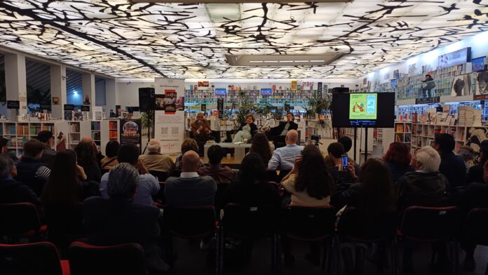 Das Bild zeigt eine Podiumsdiskussion samt Publikum in einer Bücherei. Darüber hinaus ist ein roll-up des Österreichischen Kulturforums Mexiko prominent am Podium platziert.