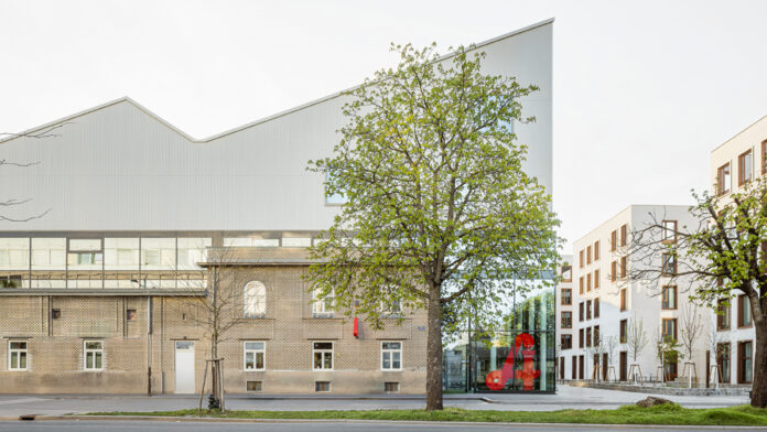 Das Bild zeigt eine moderne, langgestreckte Industriehalle mit heller Fassade.
