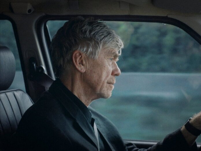 Das Bild zeigt den Schauspieler Bobby Sommer, einen älteren Mann, am Steuer eines Autos. Es handelt sich um ein Standbild aus dem Film „London“ von Sebastian Brameshuber.